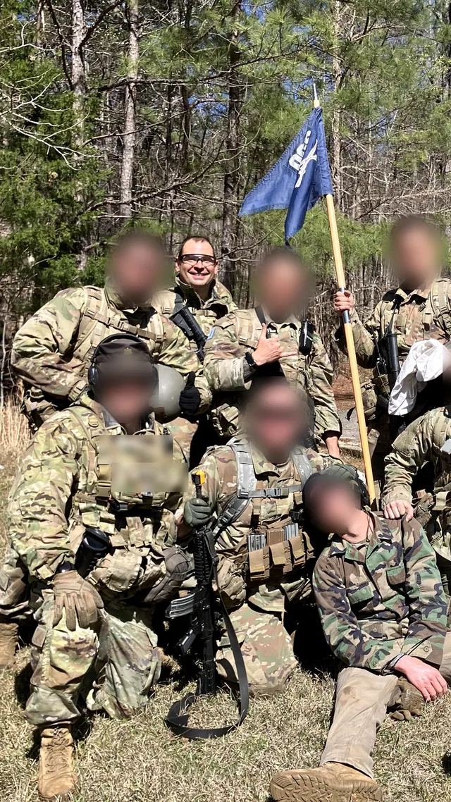 Nick Zaggy and his team in the woods beside a guidon, with others’ faces blurred.