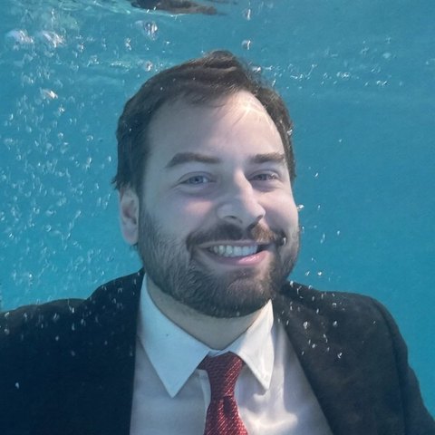 Nick Zaggy underwater in a dark suit and red tie, smiling